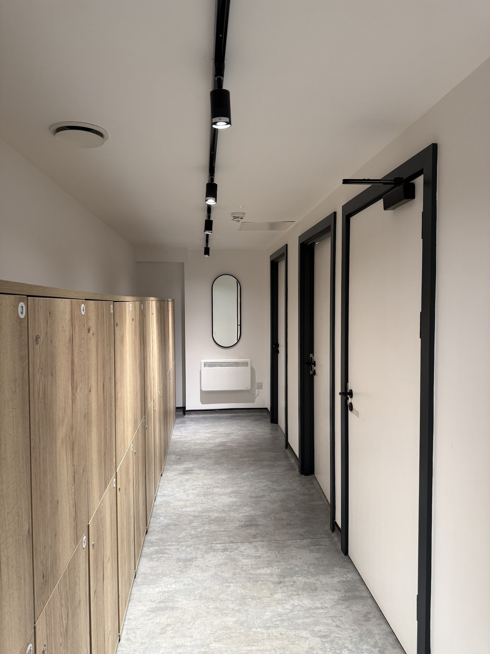 Changing room — numbered lockers, track lighting and shower rooms off the corridor