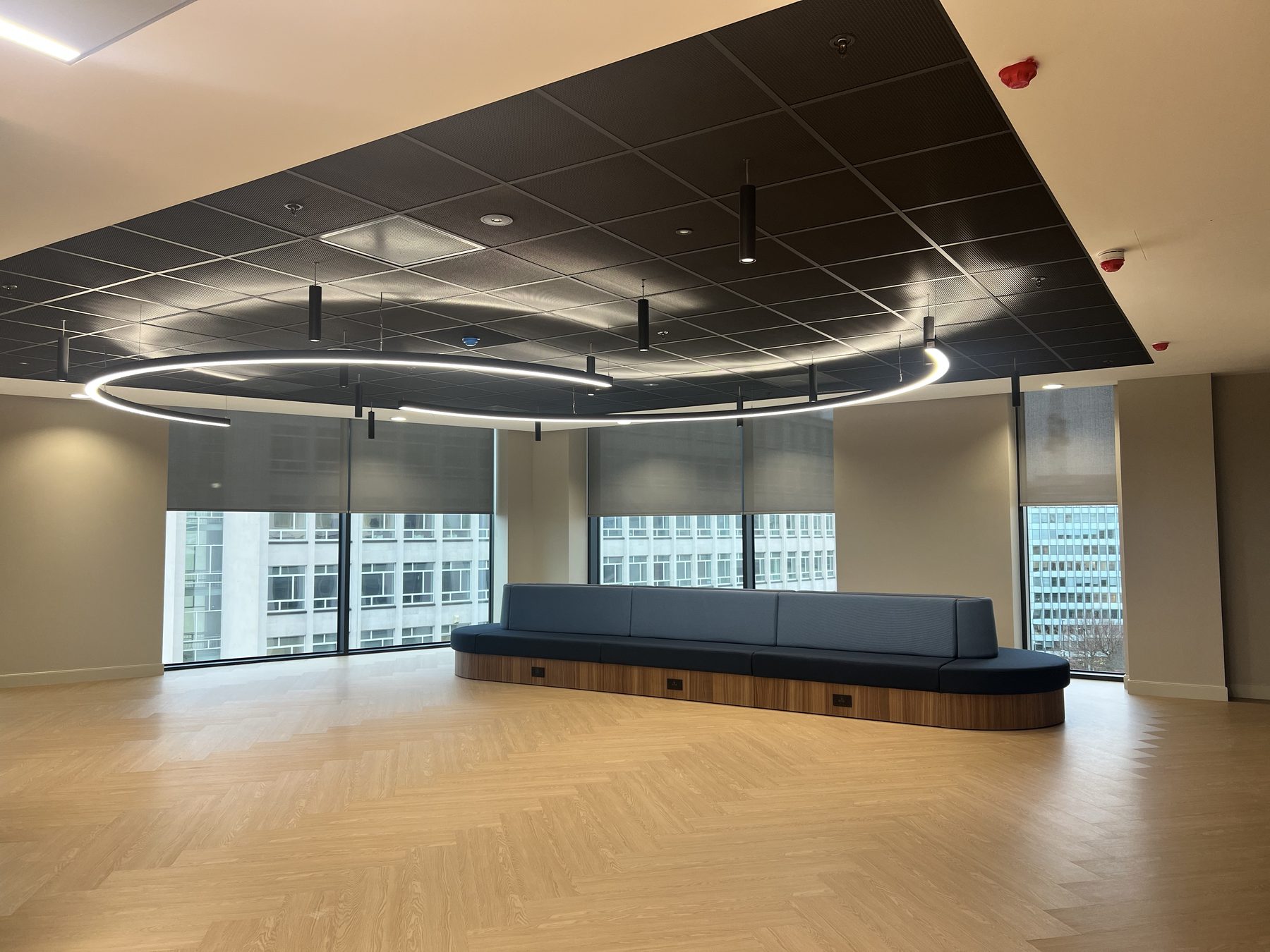 Curved banquette and herringbone oak beneath a perforated metal ceiling raft